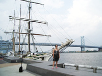 Patti in front of a sailing ship with JFK bridge to New Jersey in background